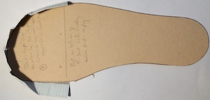 A sole-shaped piece of beige card, with white duct tape protruding upwards in the toe area.