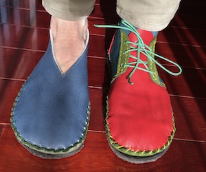 Feet wearing mis-matched shoes. On the right foot, a blue leather slipper. On the left foot, an ankle-height multi-colored boot.