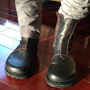 Two feet wearing calf-length black boots with red stitching.