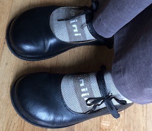 A pair of black leather court shoes with leather straps across the mid foot, fastened with black shoelaces