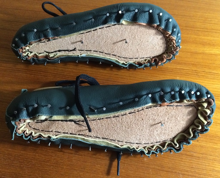 Green leather uppers tacked to lasts, seen from the underside so tack heads are clearly visible.