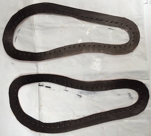 Two foot-shaped rings of leather, dyed black and punched with holes at 8mm intervals