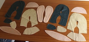 About 40 small, shaped pieces of green and beige leather laid out on a table top