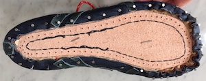 Seen from the bottom, a blue upper nailed to a shoe last.