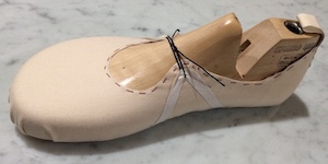 A cloth upper taped to a wooden last, attached with a black lace at midfoot