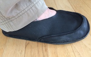 a right foot in a dark blue leather slipper with a wide toe shape.