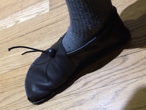 A right foot in a grey sock and soft-looking brown shoe that is distinctly foot-shaped.