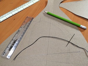 Pieces of card, a needle, and a black thread, as well as two rulers and a green pencil