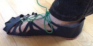 A right foot in a dark blue leather sandal attached with a green lace.