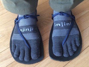 A pair of feet wearing grey wool toe socks, in huarache sandals with black rubber soles and blue lacing.