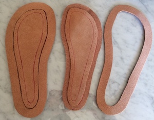 Pieces of veg tan leather marked with pen and cut out in the shape of soles