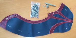 An eyelet setter lying on a table alongside two partially assembled shoe uppers with eyelets installed