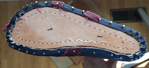 The bottom of a last with a blue/red upper and veg-tan sole nailed neatly to it