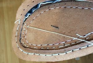 A pale thread being pulled through holes in a welt and mid-sole