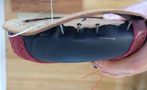 Close-up of a veg-tan welt being sewn  with 1mm thread onto a blue leather upper nailed to a last