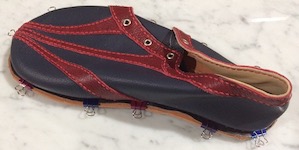 A blue and red shoe removed from the last, and clamped via a barely-visible black welt to a slightly larger piece of veg-tan leather